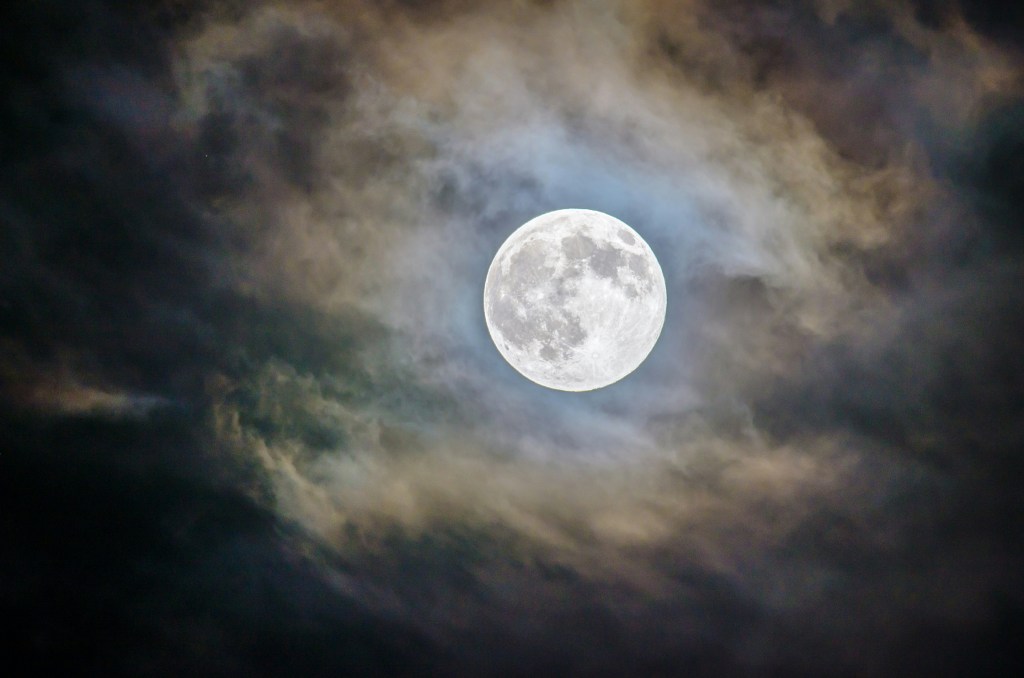 The night sky full of clouds except for the area around the bright full moon.