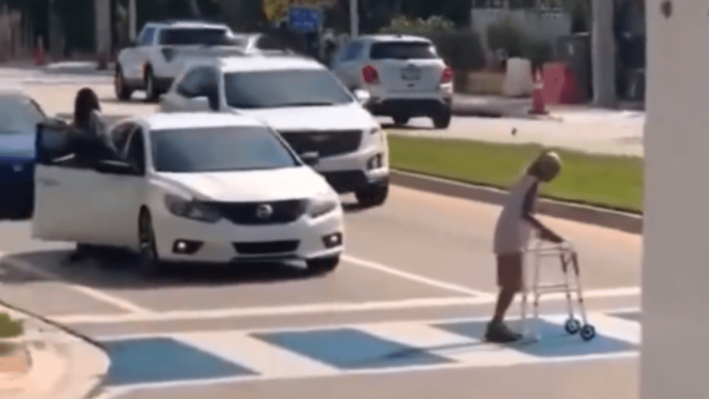 A man helps a grandma with a walker cross the road.