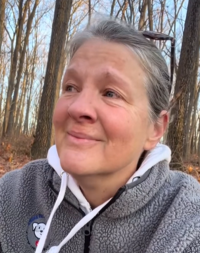 A grieving woman in the woods smiles through her tears.