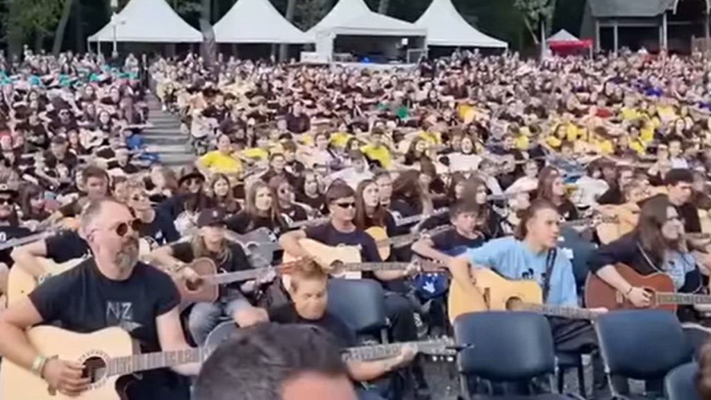 View of a massive group of people playing guitars outside at an event.