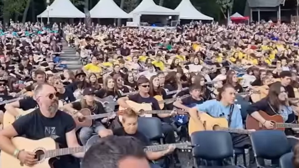 View of a massive group of people playing guitars outside at an event.