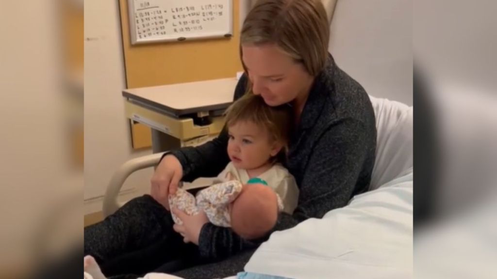 A little girl becomes a big sister and gets to hold the baby while sitting on mom's lap.