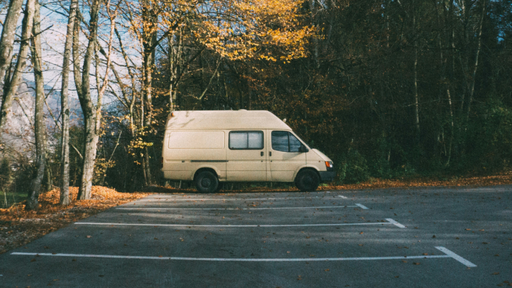 A large white van sits in an empty parking lot at a distance. Trees are nearby.