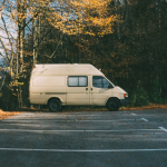 A large white van sits in an empty parking lot at a distance. Trees are nearby.