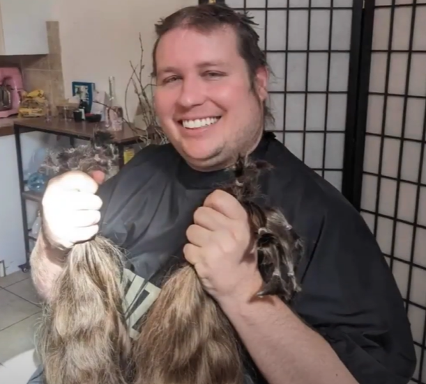 Cody smiles as he holds his freshly cut hair in his hands.