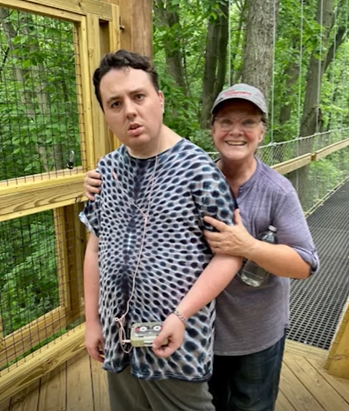 A mom and her son walking outdoors surrounded by trees.