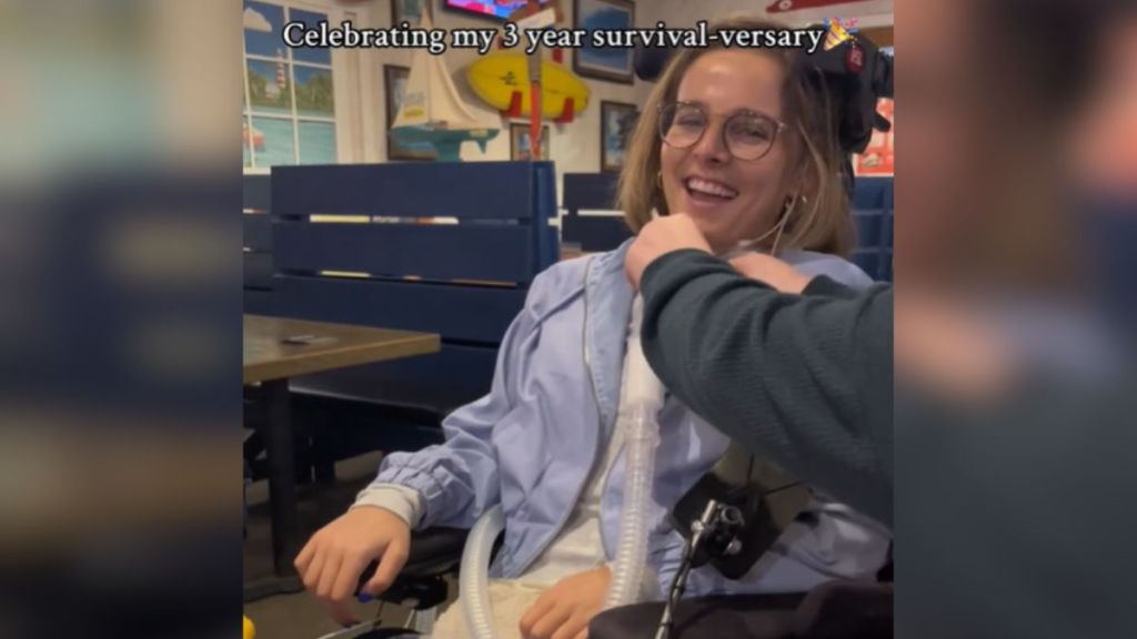 A woman on a breathing tube in a powerchair laughs.