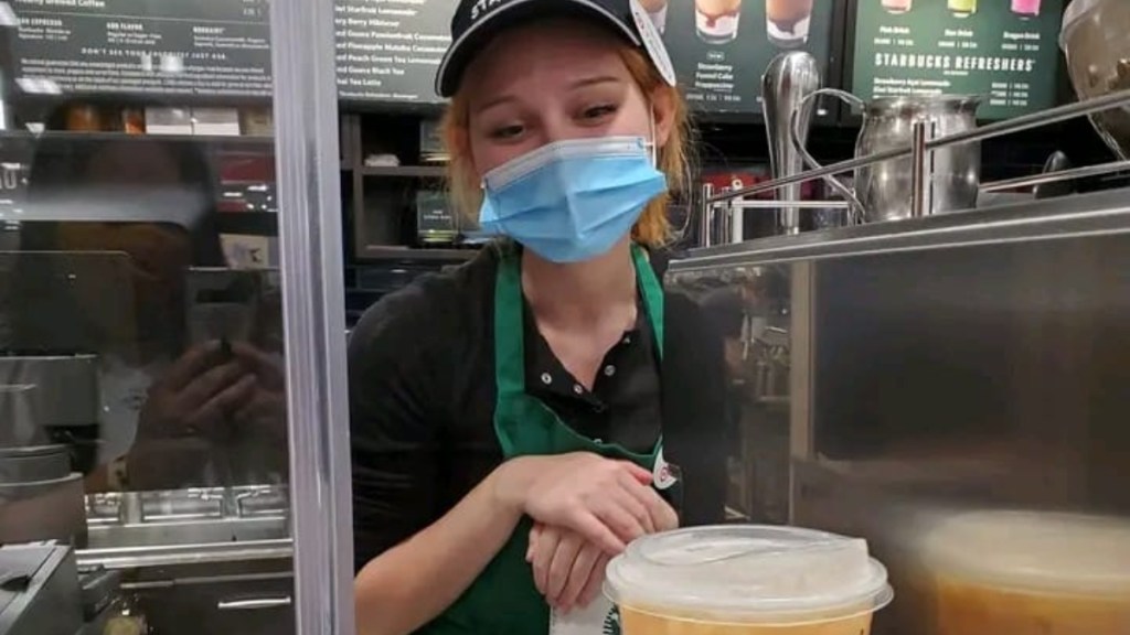 A Starbucks barista who is wearing a mask shyly looks down and smiles at the drink she made for someone who just went through a breakup.