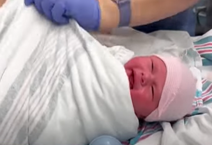 A newborn baby wrapped in a white blanket.