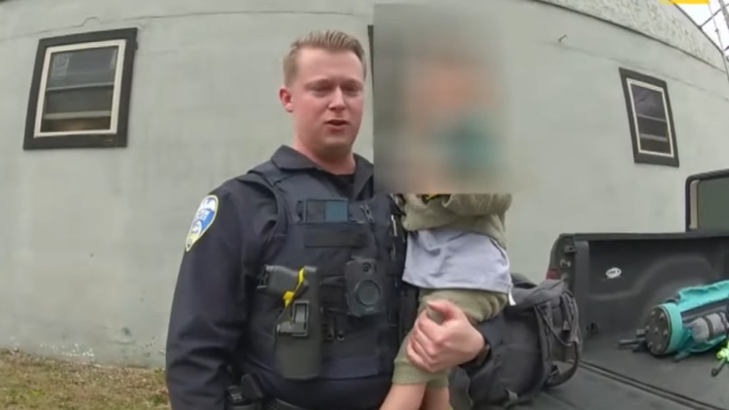 An officer holds a toddler in his arms after saving him from a carjacking.