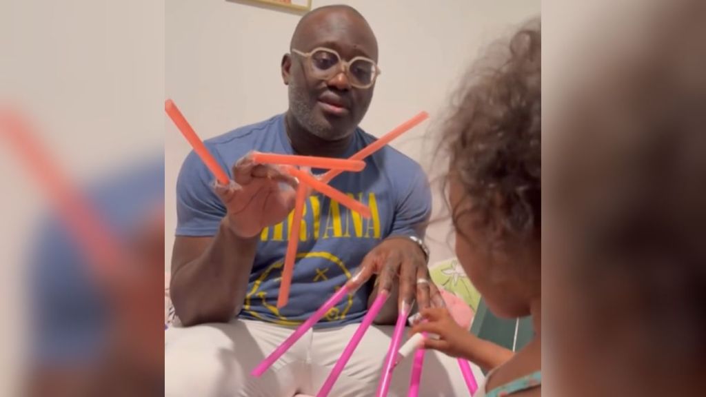 A dad with straws taped to his nails plays pretend with his toddler.