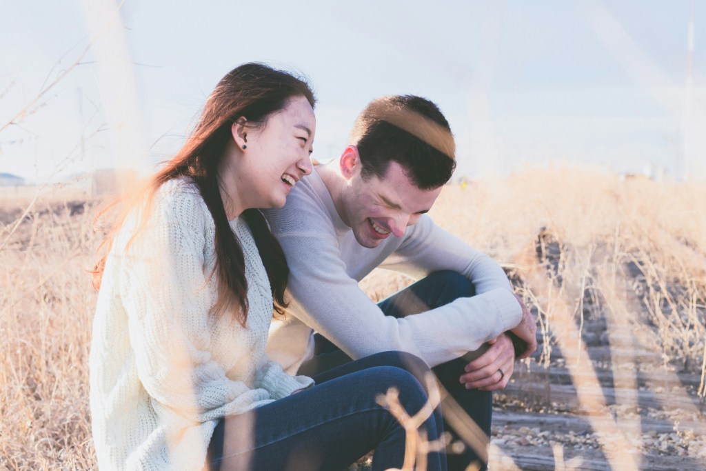 A couple laughing together while sitting outdoors.