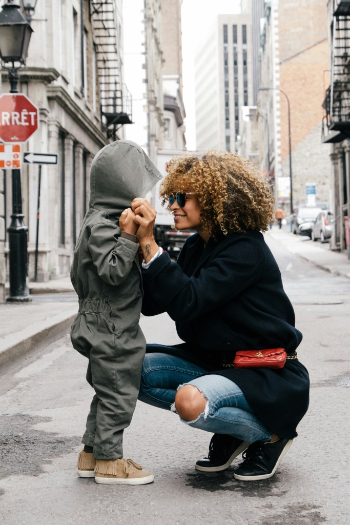 A woman crouching down and smiling at a child.