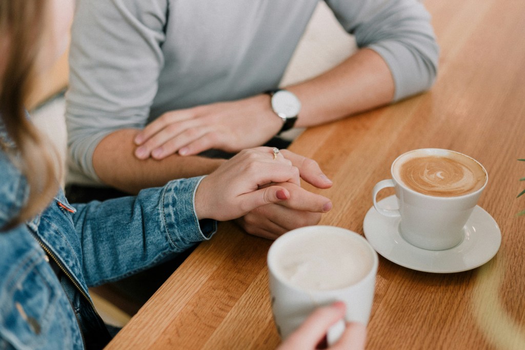 A couple holding hands while having coffee. 