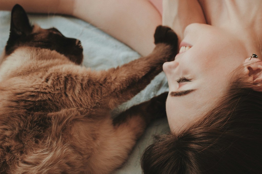A woman laying down next to a cat with her eyes closed. 