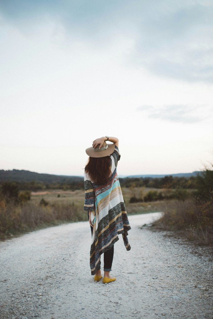 A woman walking in nature while holding onto her hat.