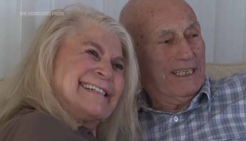 Close up of Harold Terens and Jeanne Swerlin smile as they sit closely on a couch.
