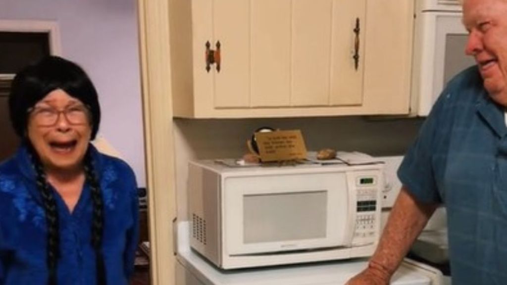 Image shows an elderly couple laughing at the grandma trying on wigs during cancer treatments.