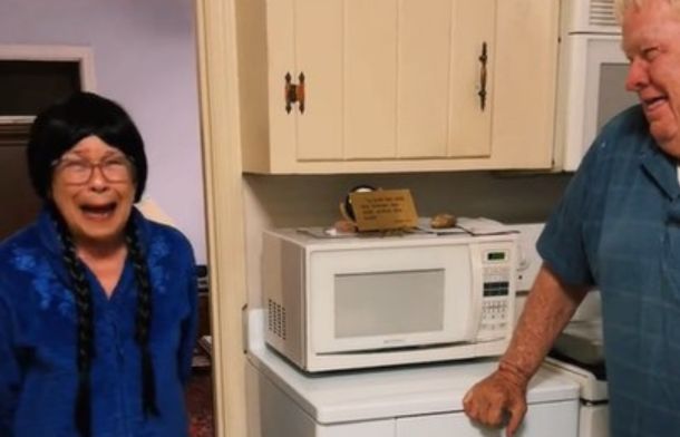 Image shows an elderly couple laughing at the grandma trying on wigs during cancer treatments.