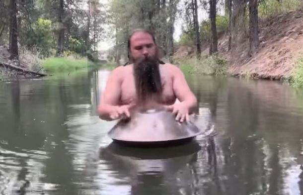 Ethereal in E plays the handpan drum while it rests on water in a small river.