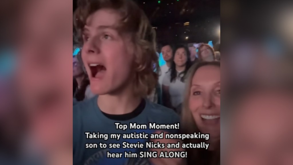 A mom smiles wide as she records her son singing at a concert. Text on the image: Top Mom Moment! Taking my autistic and nonspeaking son to see Stevie Nicks and actually hear him SING ALONG!