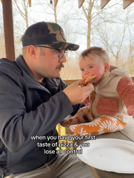A baby tries pizza given to her by her dad.