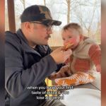 A baby tries pizza given to her by her dad.