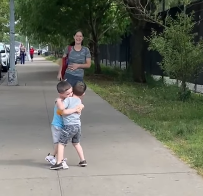 Two little kids who are best friends hugging on the sidewalk.