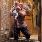 A grandpa picks up his baby grandson on the stoop.