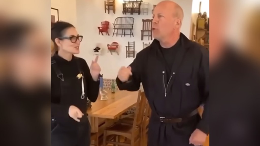 Bruce Willis and Demi Moore smile as they start to dance together in a dining room.