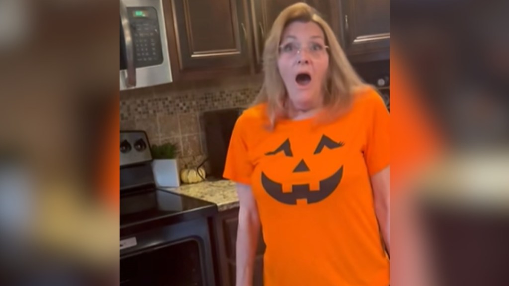 A woman looks shocked, mouth open, as she stands in front of an open oven.