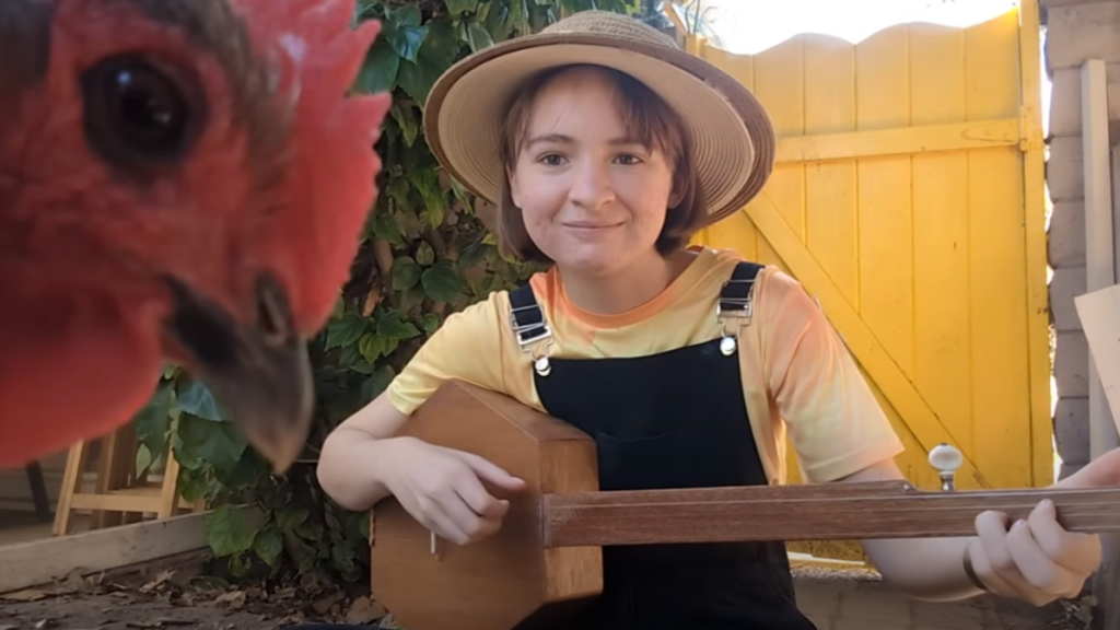 Phoebe Sanders plays a fretless banjo while her chicken, Ozma, checks out the camera.