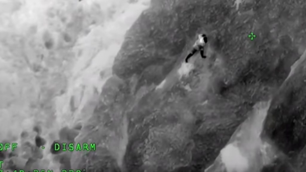 Thermal imaging of a man hanging onto the side of a cliff.