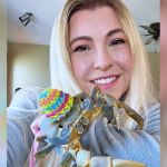 A blonde woman holding her pet crab, who is wearing a hat.