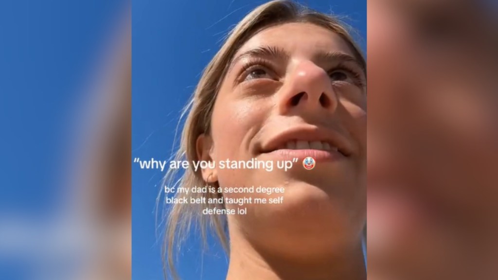 Close up of a woman smirking as she looks at someone we can't see. Text on the image reads: "why are you standing up" Clown emoji. bc my dad is a second degree black belt and taught me self defense lol
