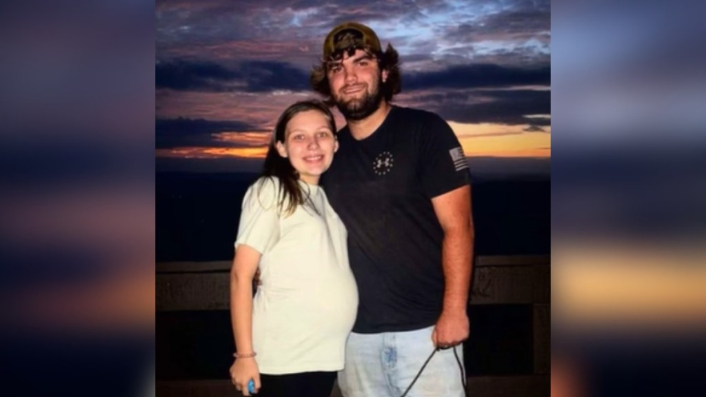 A pregnant woman and man smile as they pose outside at night soon after they stared dating. A sunset can be seen in the distance.