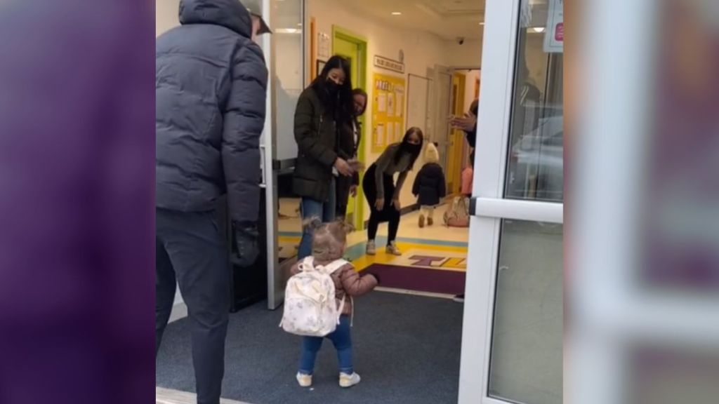 A little girl walking into a daycare center where caregivers are waiting for her.