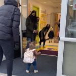 A little girl walking into a daycare center where caregivers are waiting for her.