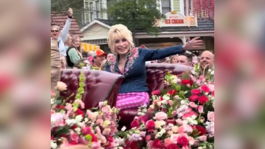 Dolly Parton smiles wide as she waves at fans from a carriage.