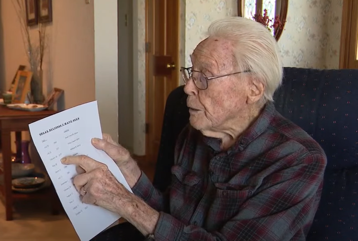 An elderly man points to a list on a piece of paper.