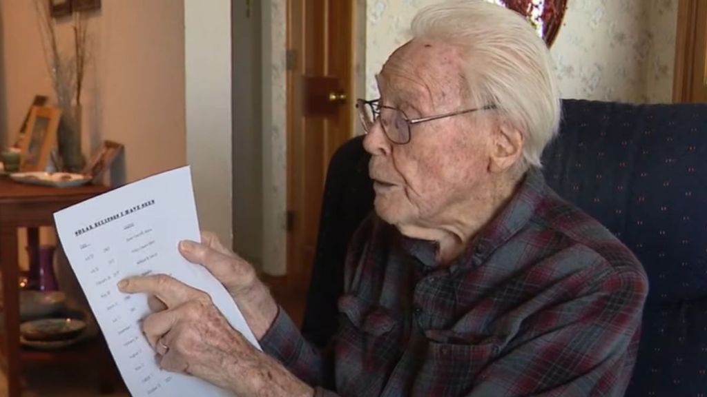 An elderly man points to a list on a piece of paper.