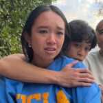 A teen gathers outside to sit on the ground with her brother, mom, and dad. The teen has tears in her eyes as her brother hugs her from behind. Mom and dad also look devastated.
