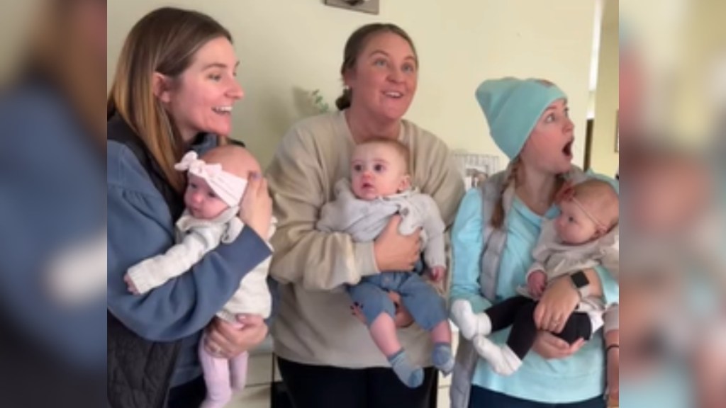 Three women stand next to each other, each holding a baby. All three look surprised in different ways.