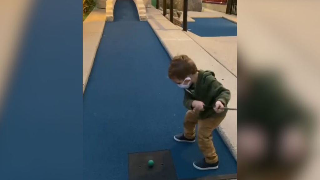 A toddler playing mini golf in a green hoodie.
