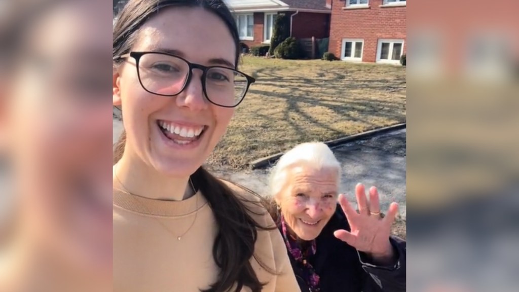 A woman smiles as she and her Nonna walk outside. Nonna smiles and waves at the camera.