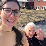 A woman smiles as she and her Nonna walk outside. Nonna smiles and waves at the camera.