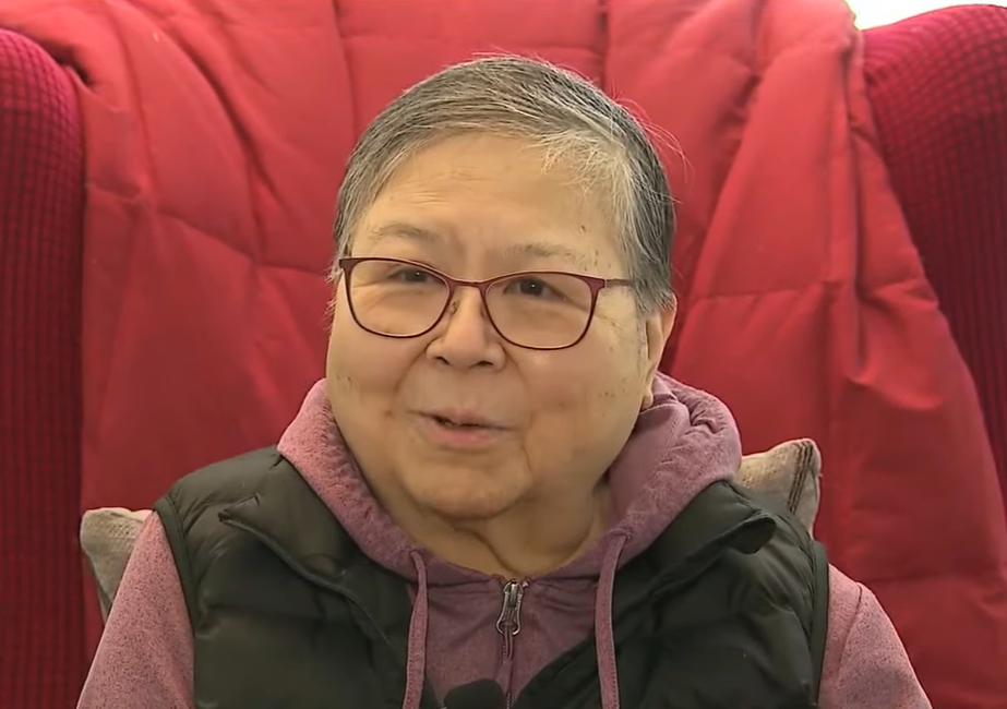 Lily Woo smiles as she talks to news crew while sitting in a red chair.