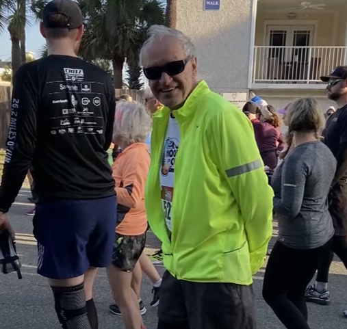 An elderly man wears a green jacket during a half marathon.