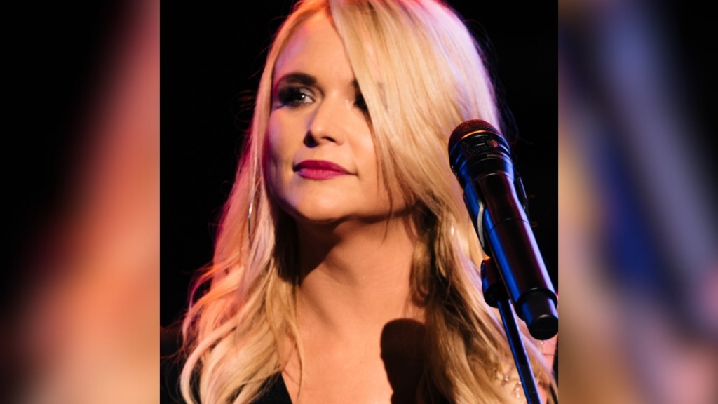 Close up of Miranda Lambert as she stands in front of a mic. Her head is turned slightly as she looks out into the crowd.