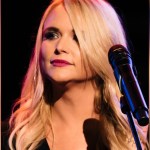 Close up of Miranda Lambert as she stands in front of a mic. Her head is turned slightly as she looks out into the crowd.